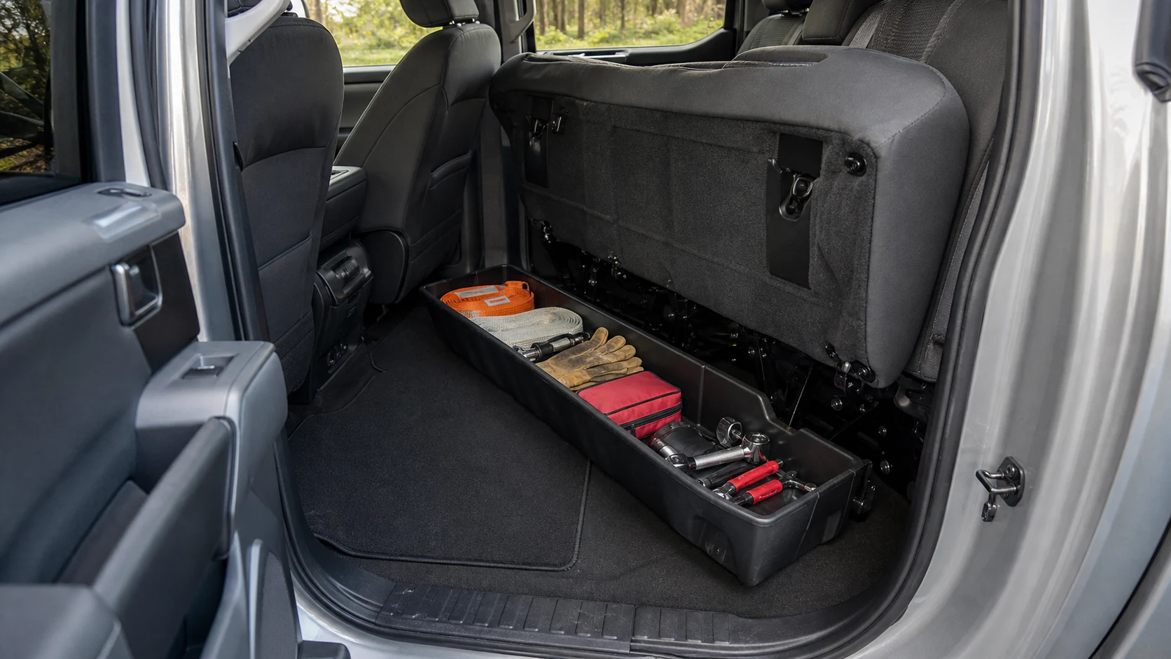 Pickup rear bench lifted above a molded under-seat storage bin with organized tools
