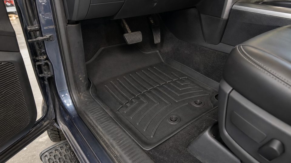 Pickup driver footwell with one molded floor mat secured to two retainers below clear brake and accelerator pedals