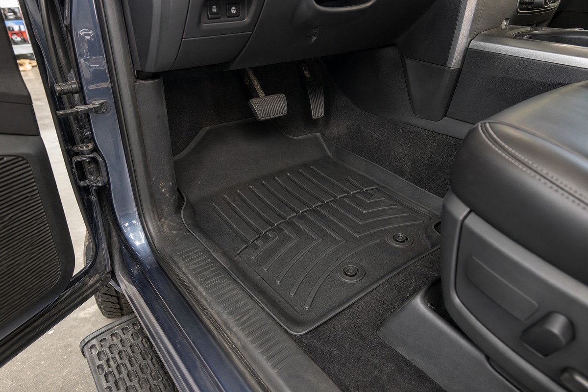 Pickup driver footwell with one molded floor mat secured to two retainers below clear brake and accelerator pedals